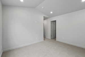 Carpeted empty room with vaulted ceiling and recessed lighting