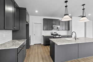 Kitchen with decorative light fixtures, stainless steel appliances, light wood finished floors, and backsplash
