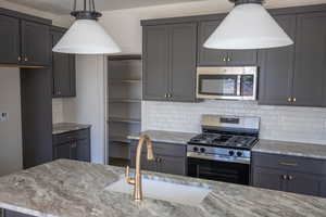 Kitchen featuring stainless steel appliances, backsplash, light stone counters, and gray cabinetry