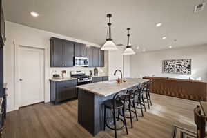 Kitchen featuring light stone countertops, a kitchen breakfast bar, decorative light fixtures, a center island with sink, and open floor plan