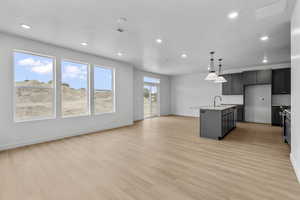 Kitchen with a center island with sink, hanging light fixtures, open floor plan, light wood-type flooring, and backsplash