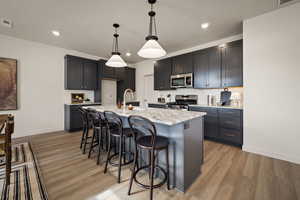 Kitchen with hanging light fixtures, a breakfast bar, light stone countertops, stainless steel appliances, and light wood finished floors