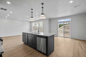 Kitchen with pendant lighting, stainless steel dishwasher, a center island with sink, light stone counters, and light wood-style flooring