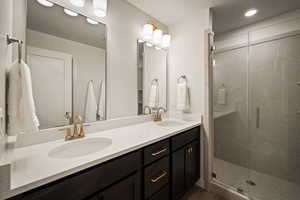 Full bathroom featuring double vanity, a marble finish shower, and recessed lighting