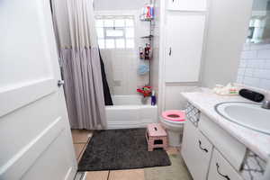 Full bathroom with vanity, shower / bathtub combination with curtain, and light tile patterned floors