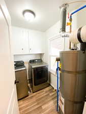 Laundry room with secured water heater, light wood-style floors, independent washer and dryer, and cabinet space