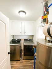 Laundry room featuring water heater, light wood-style floors, cabinet space, and separate washer and dryer
