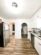 Kitchen featuring decorative backsplash, appliances with stainless steel finishes, arched walkways, and white cabinetry