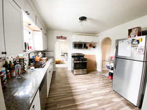 Kitchen with stainless steel appliances, white cabinetry, arched walkways, decorative backsplash, and light wood-style floors