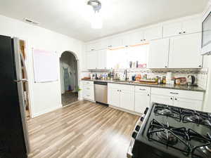 Kitchen featuring stainless steel appliances, white cabinetry, arched walkways, decorative backsplash, and dark stone counters