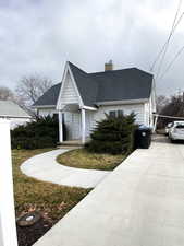 View of front facade with roof with shingles, a chimney, and concrete driveway