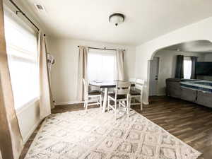 Dining space with dark wood finished floors, plenty of natural light, and arched walkways