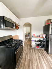 Kitchen featuring appliances with stainless steel finishes, arched walkways, light wood finished floors, and white cabinets
