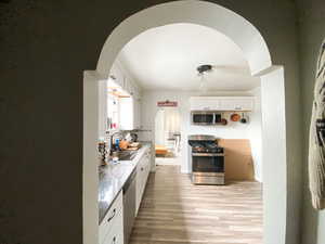 Kitchen featuring white cabinetry, appliances with stainless steel finishes, arched walkways, light wood-style flooring, and decorative backsplash