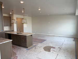 Kitchen featuring light stone counters, a center island with sink, dark wood finish cabinets, recessed lighting, and open floor plan