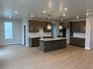 Kitchen with dark wood finish cabinetry, an island with sink, backsplash, and light stone countertops