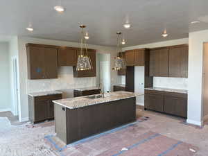 Kitchen with tasteful backsplash, dark wood finish cabinets, an island with sink, and light stone counters