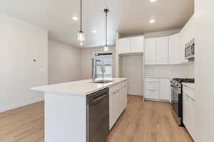 Kitchen with white cabinets, modern cabinets, stainless steel appliances, hanging light fixtures, and light wood-style flooring