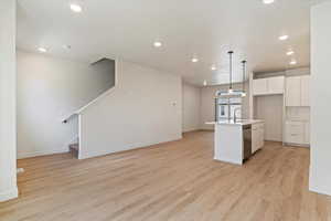 Kitchen featuring a center island with sink, white cabinetry, hanging light fixtures, light wood finished floors, and open floor plan