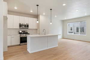 Kitchen with stainless steel appliances, hanging light fixtures, white cabinetry, and light wood finished floors