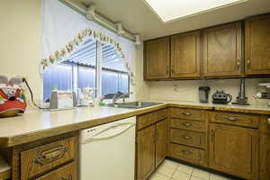 Kitchen featuring white dishwasher, light countertops, light tile patterned floors, and wood finish cabinetry