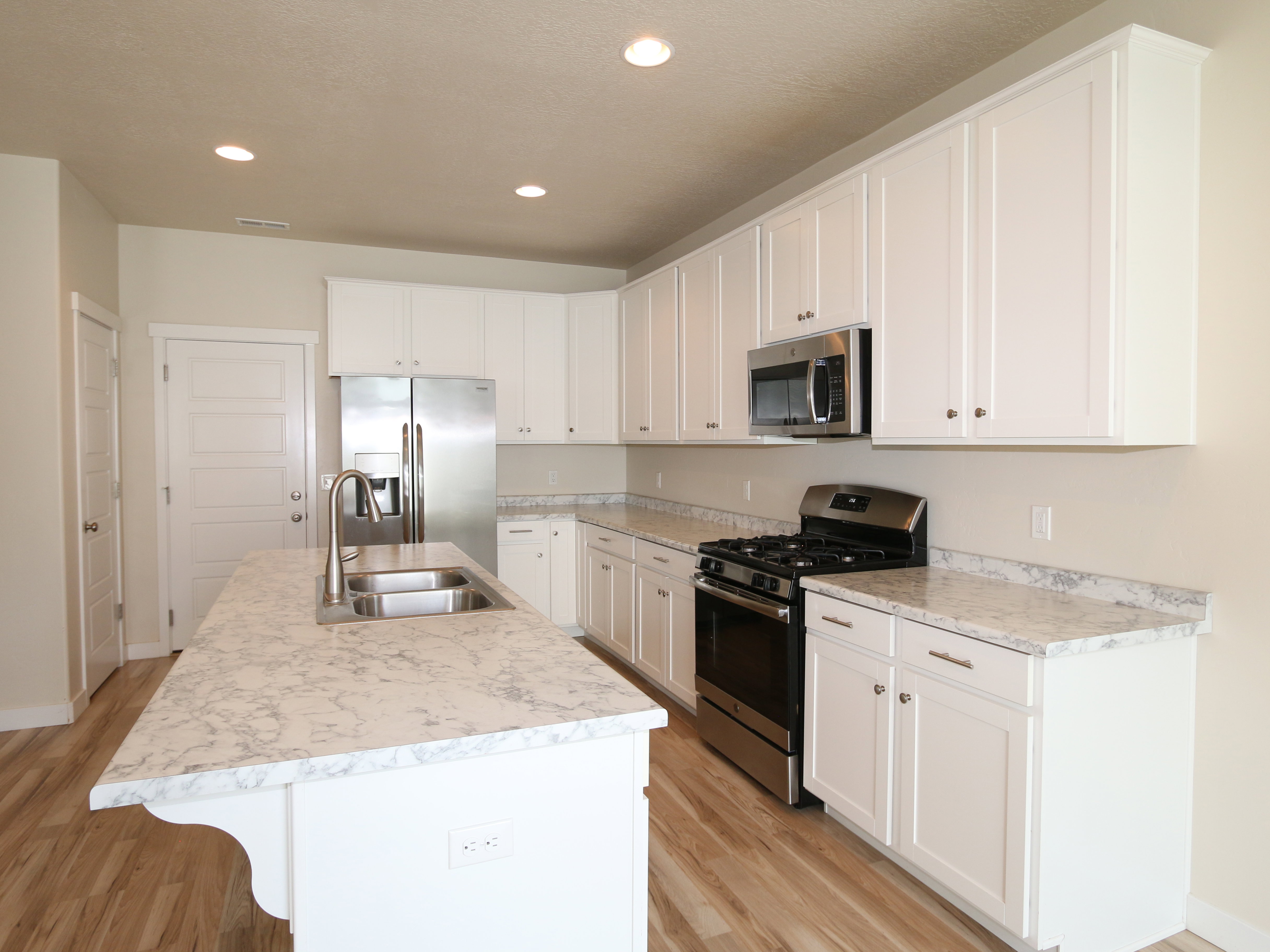 Kitchen featuring stainless steel appliances, light countertops, white cabinetry, a kitchen island with sink, and light wood finished floors
