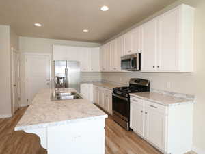 Kitchen featuring stainless steel appliances, light countertops, white cabinetry, a kitchen island with sink, and light wood finished floors