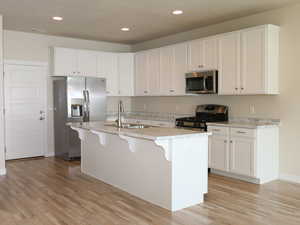 Kitchen featuring stainless steel appliances, white cabinetry, a breakfast bar area, light wood finished floors, and recessed lighting