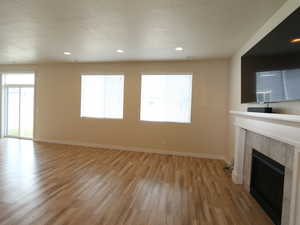 Unfurnished living room featuring a tile fireplace, recessed lighting, light wood-type flooring, a textured ceiling, and healthy amount of natural light