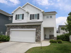 Craftsman-style home with stone siding, an attached garage, board and batten siding, concrete driveway, and a shingled roof