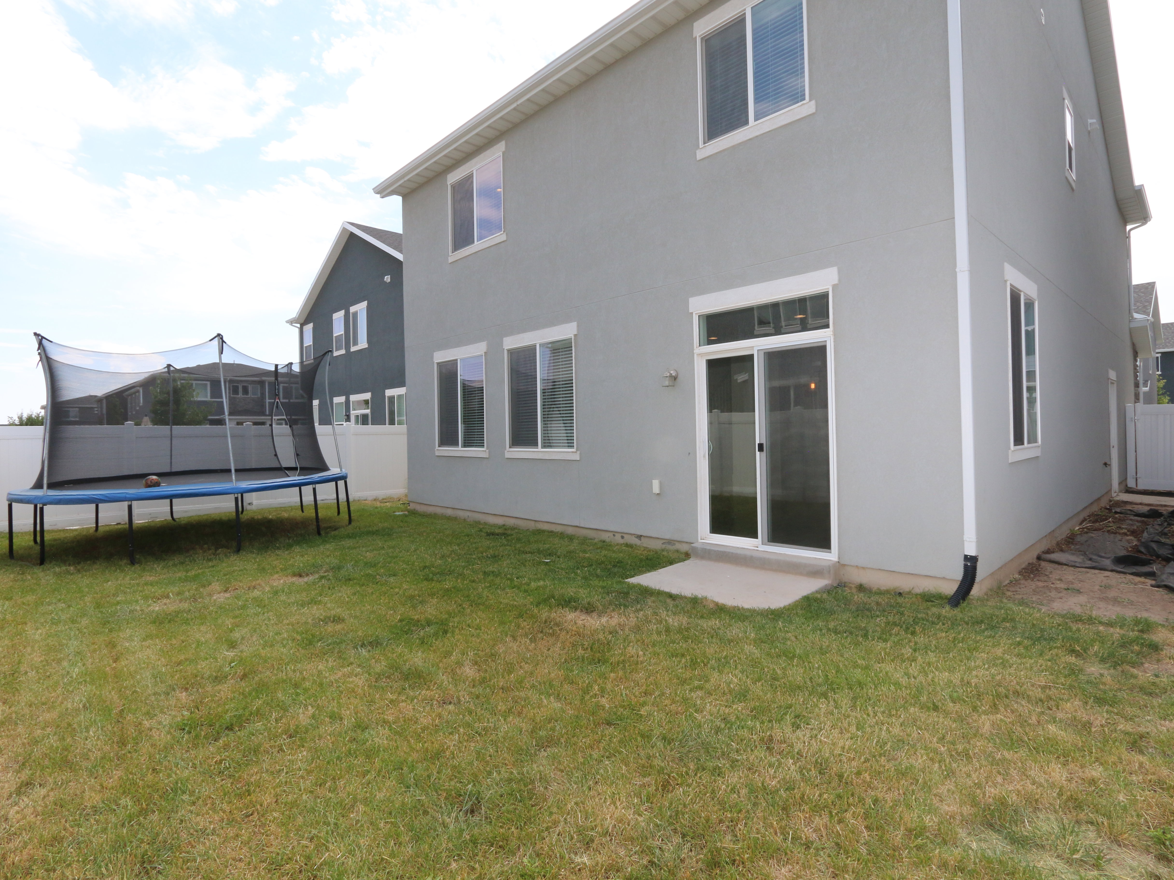 Back of property with a fenced backyard, a trampoline, and stucco siding
