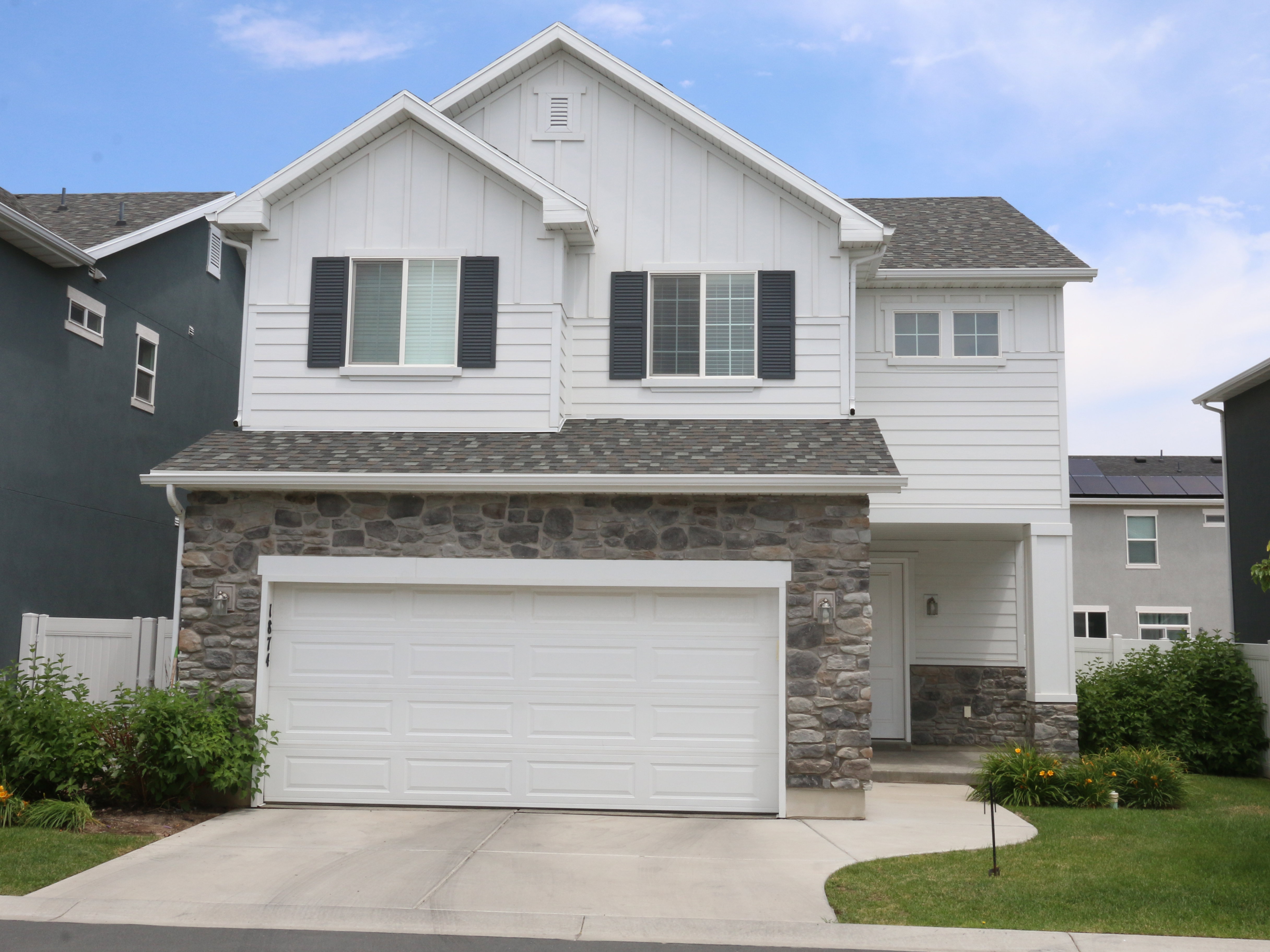 View of front facade with board and batten siding, stone siding, an attached garage, driveway, and roof with shingles
