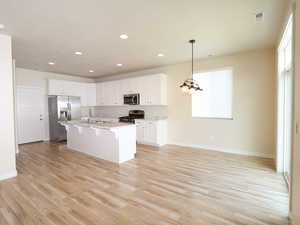 Kitchen featuring stainless steel appliances, a breakfast bar area, a kitchen island with sink, white cabinetry, and light wood finished floors