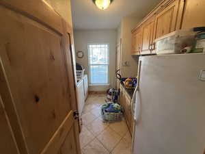 Kitchen with freestanding refrigerator, light tile patterned floors, washer and dryer, and a textured ceiling