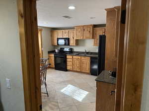 Kitchen with black appliances, recessed lighting, a textured ceiling, light tile patterned floors, and dark stone counters