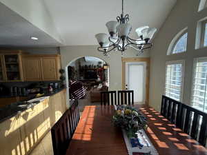 Dining space with arched walkways, a chandelier, and vaulted ceiling