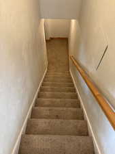 Staircase featuring a textured wall and carpet flooring