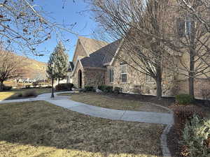 View of property exterior with a lawn, stone siding, and a shingled roof