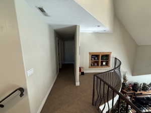 Hallway featuring an upstairs landing, carpet floors, and a textured ceiling