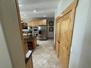 Kitchen with a textured wall, stainless steel appliances, light tile patterned floors, a textured ceiling, and dark stone countertops