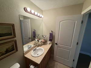 Half bath featuring a textured wall, a textured ceiling, vanity, and light tile patterned floors