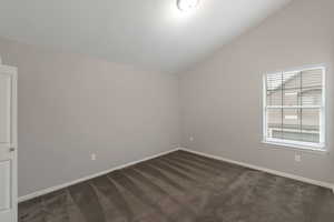 Empty room featuring lofted ceiling and dark carpet