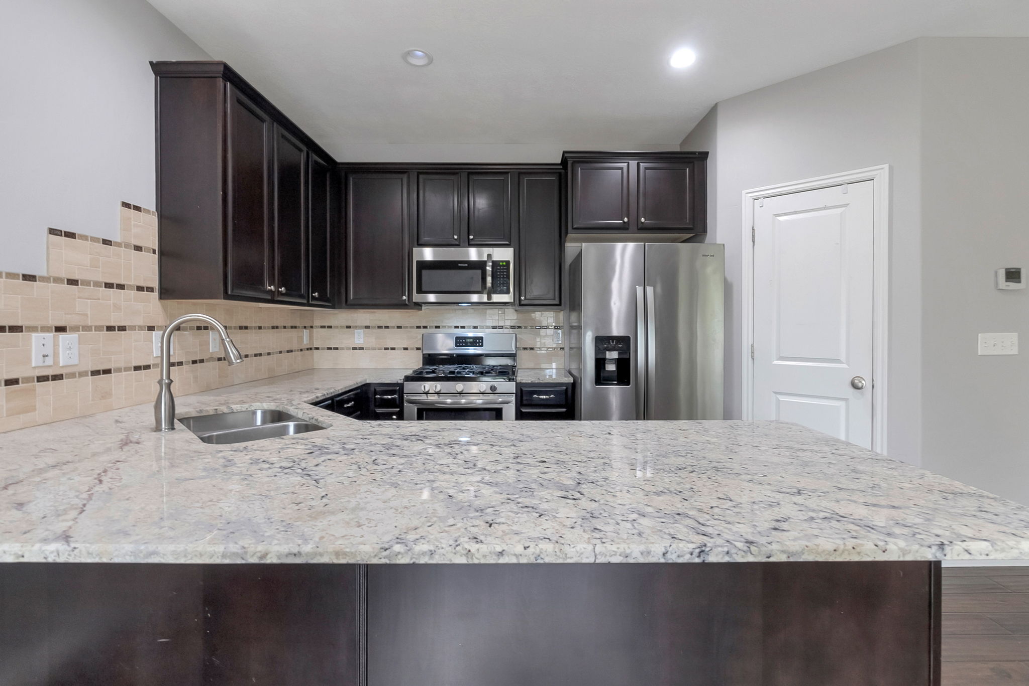 Kitchen with stainless steel appliances, light stone counters, dark wood finish cabinetry, and a peninsula
