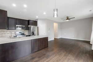 Kitchen featuring light stone counters, stainless steel appliances, pendant lighting, backsplash, and dark wood-style flooring