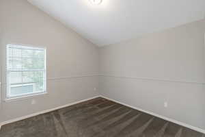 Empty room with vaulted ceiling and dark carpet