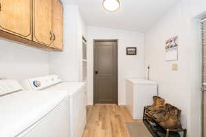 Laundry room with light wood-style flooring, washer and clothes dryer, and cabinet space