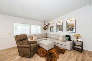 Living room with a decorative wall, light wood finished floors, and lofted ceiling