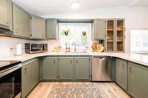 Kitchen featuring stainless steel appliances, green cabinets, light countertops, and vaulted ceiling with beams