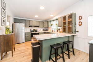 Kitchen featuring a breakfast bar area, stainless steel appliances, light countertops, light wood-style flooring, and a peninsula