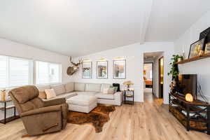 Living area with light wood finished floors and vaulted ceiling with beams